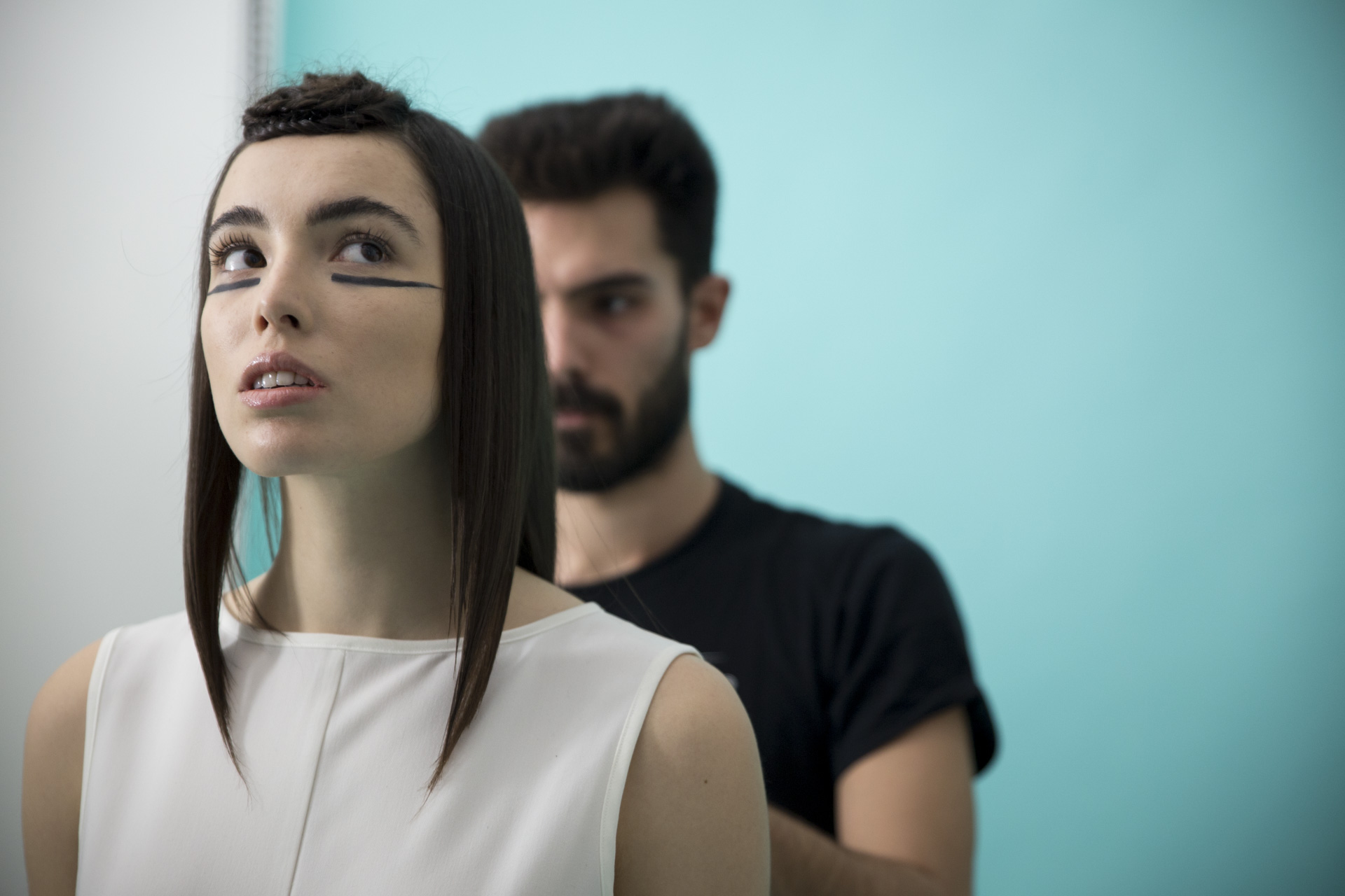 ragazza con capelli nera e canotta bianca viene pettinata da parrucchiere con t-shirt nera
