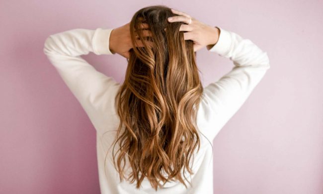 ragazza con capelli lunghi ondulati castano chiaro di spalle si tocca i capelli