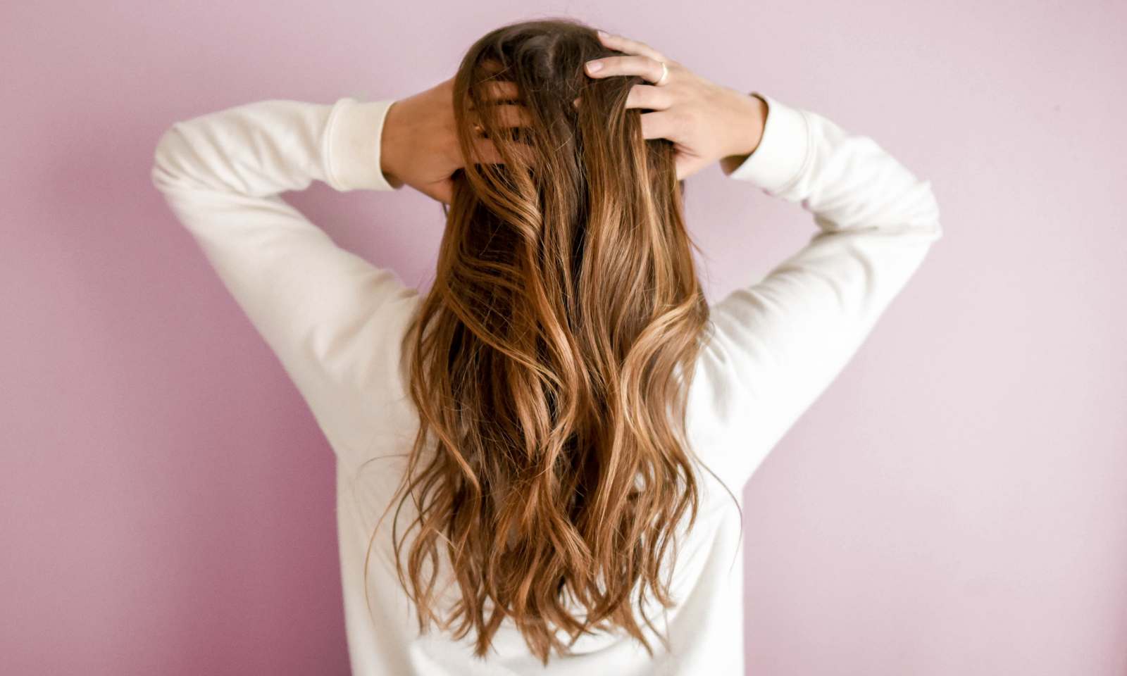 ragazza con capelli lunghi ondulati castano chiaro di spalle si tocca i capelli