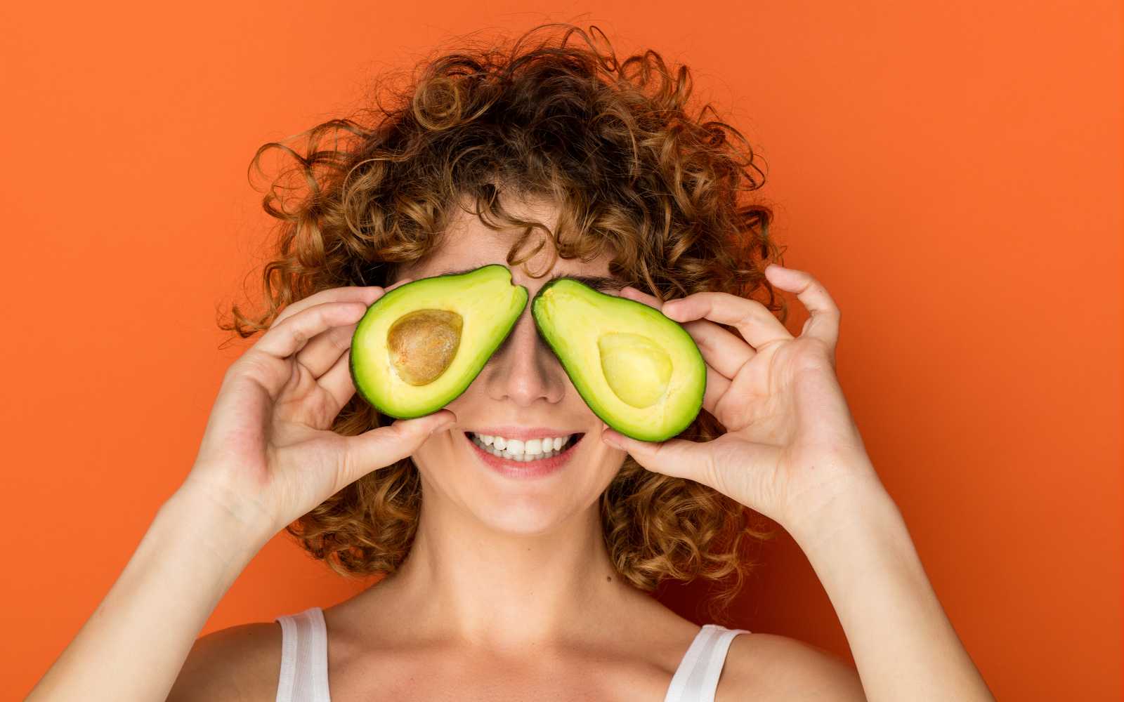 ragazza con capelli ricci tiene in mano un avocado aperto a metà