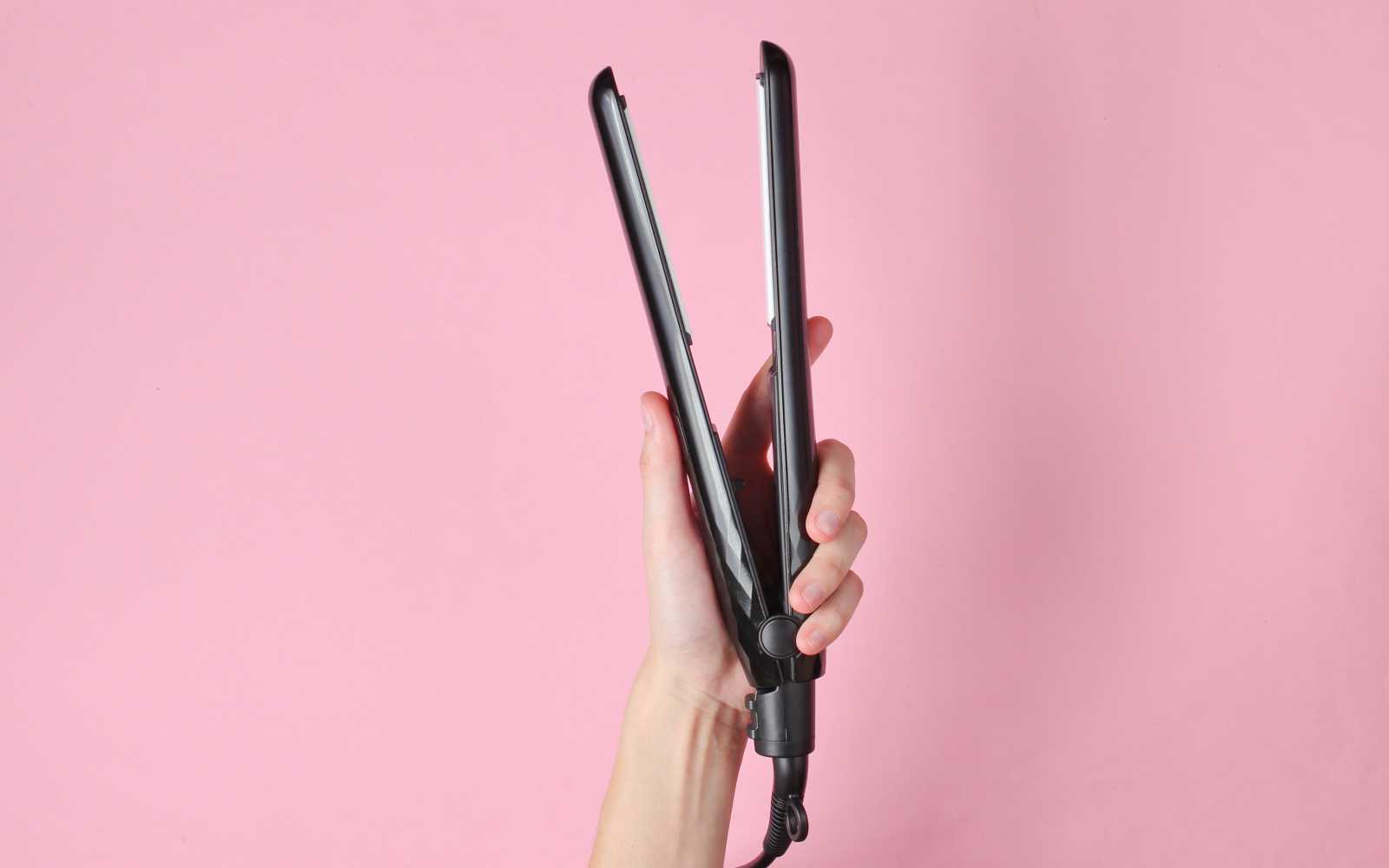 piastra per capelli nera su sfondo rosa