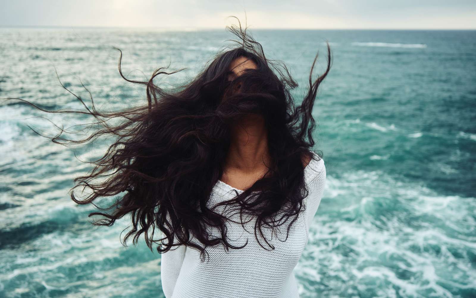 ragazza mora al mare con capelli rovinati al vento