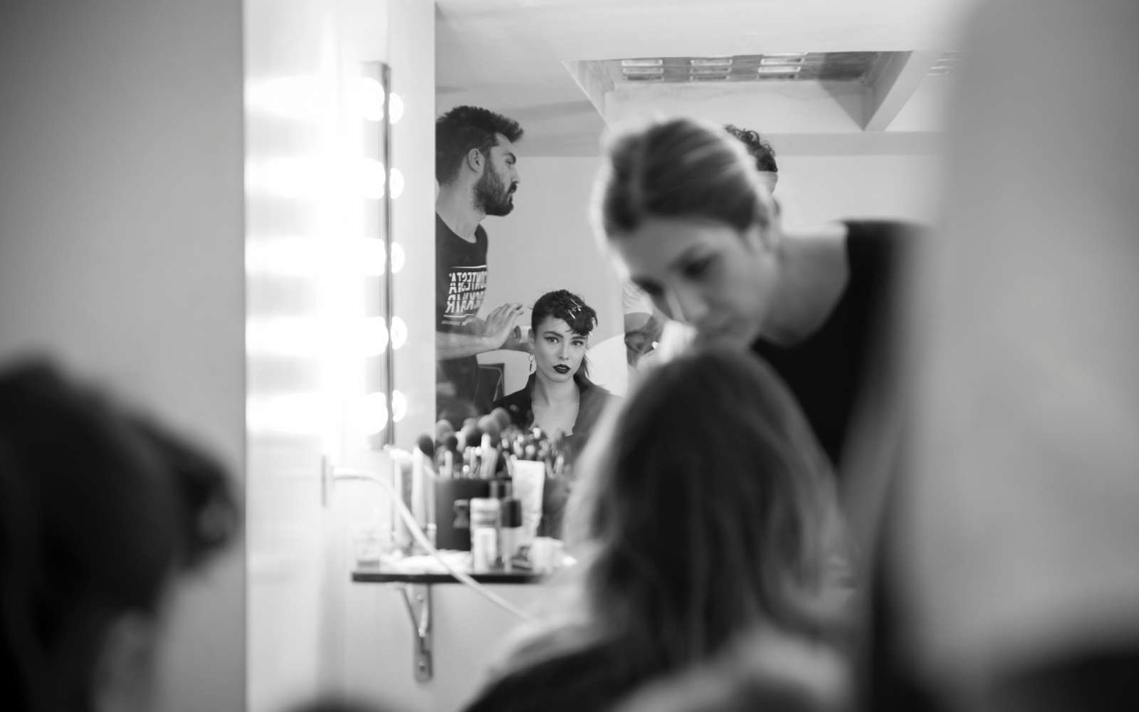 ragazza mora con viso triangolare viene pettinata e truccata da un hairstylist e una truccatrice