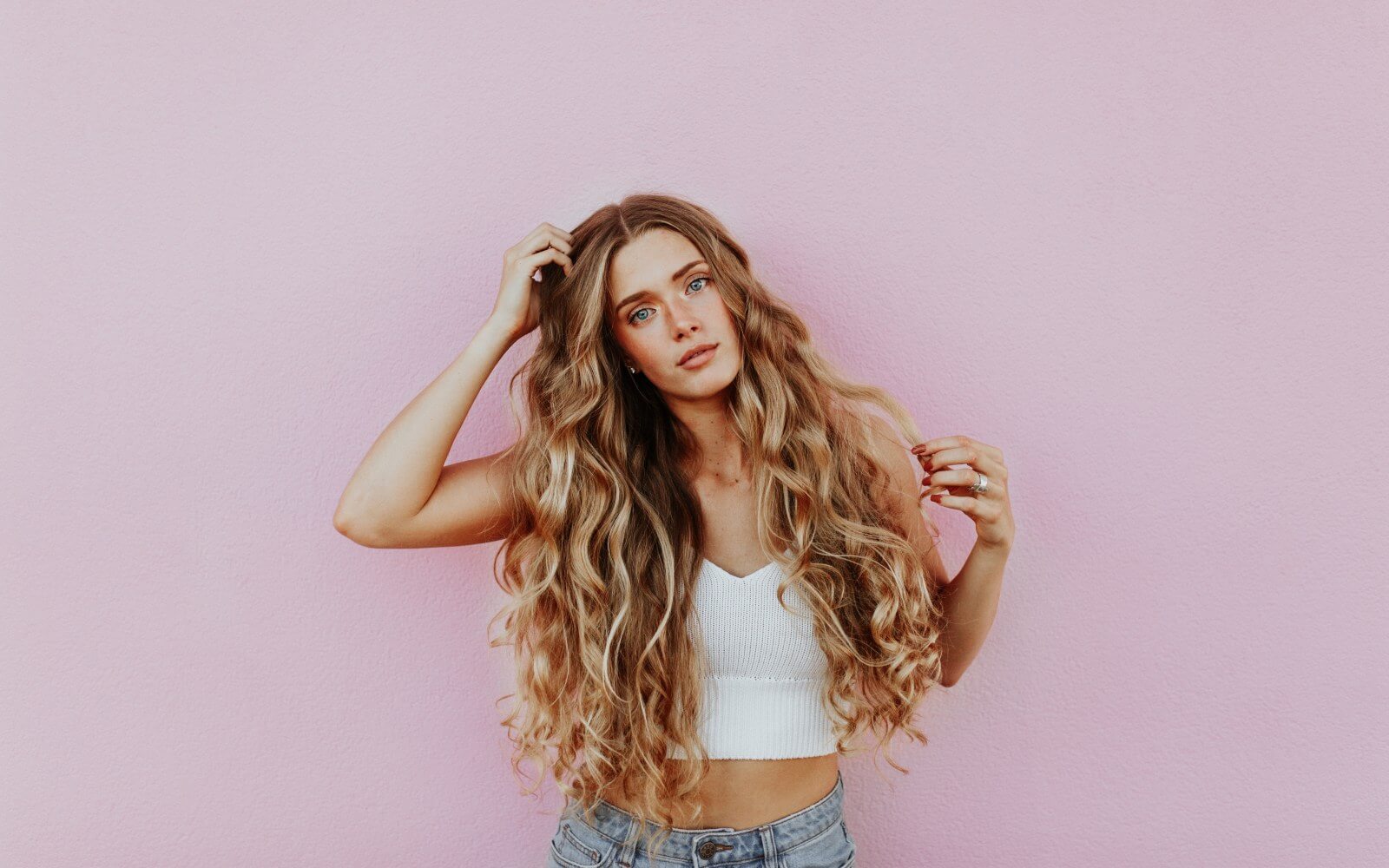 ragazza bionda con capelli ricci folti lunghi su sfondo rosa