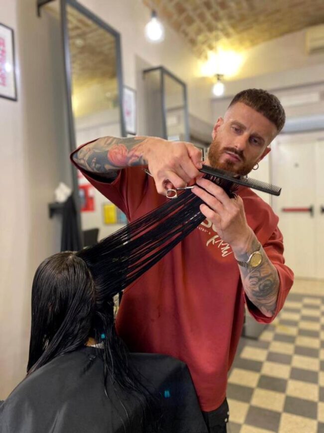 ragazzo con t-shirt rossa e tatuaggi sulla braccia taglia i capelli a ragazza mora