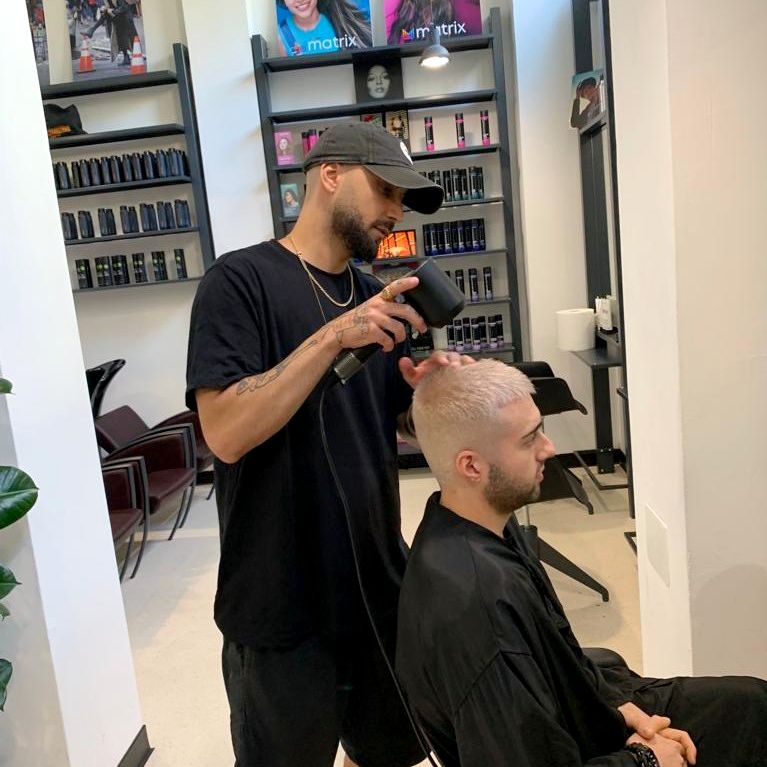 ragazzo stylist di contestarockhair in salone vestito di nero con cappello nero, asciuga capelli a ragazzo con rasatura 